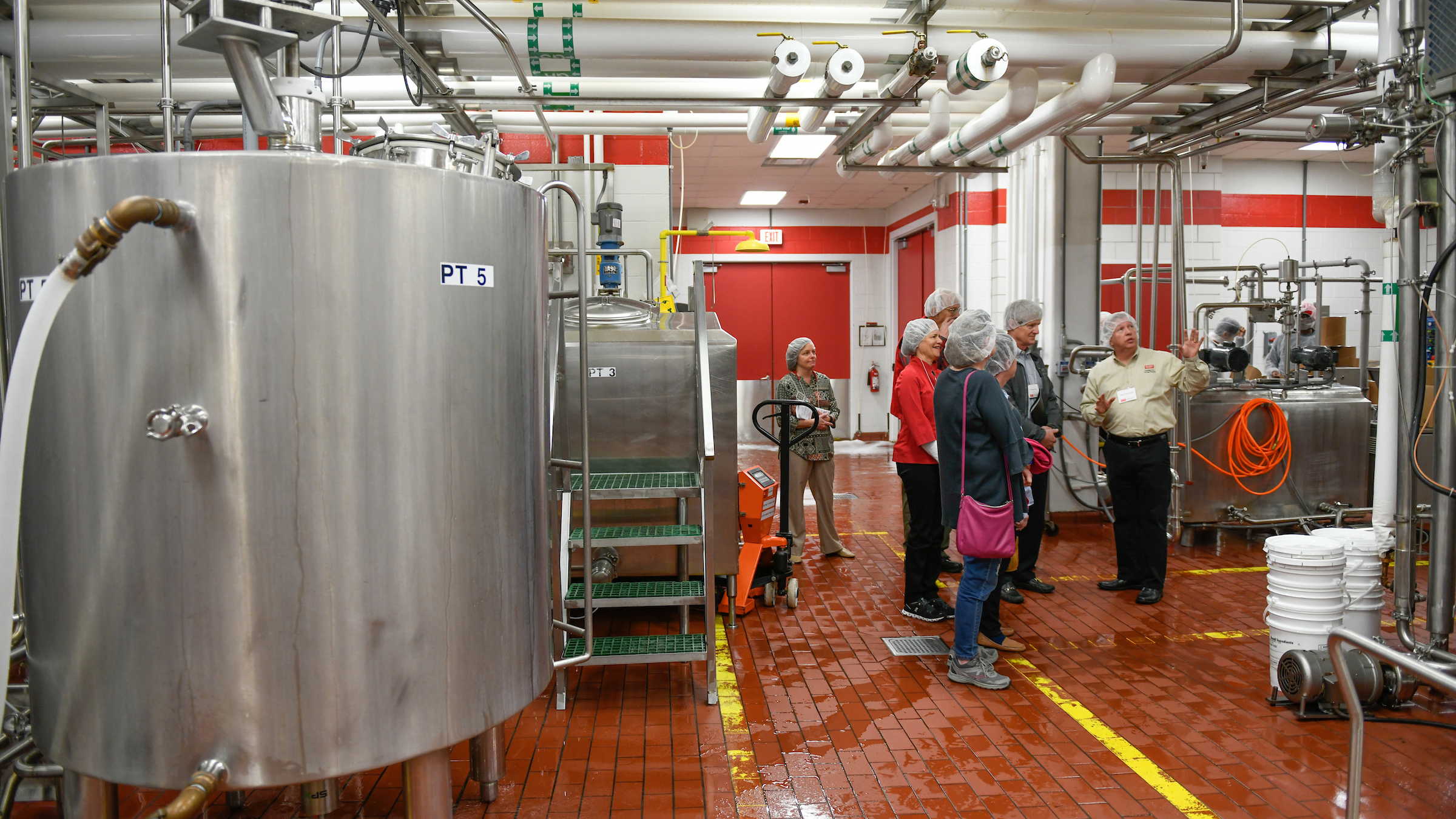 Group of people wearing hair nets tour a dairy production facility.
