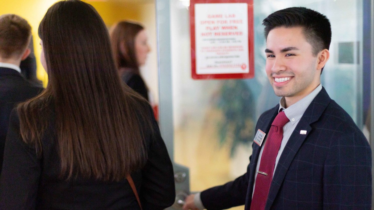 Header for news post - MMB student Alex Rojas holding a door open for fellow students